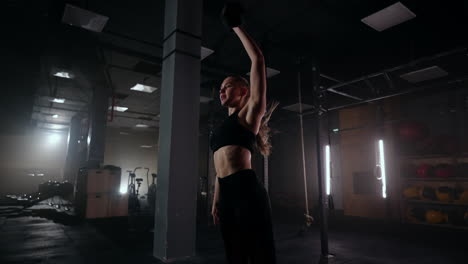 A-strong-woman-makes-efforts-and-overcoming-difficulties-lifts-a-dumbbell-in-a-dark-gym.-Fitness-woman-lifting-weight-dumbbells-training-in-gym-club.